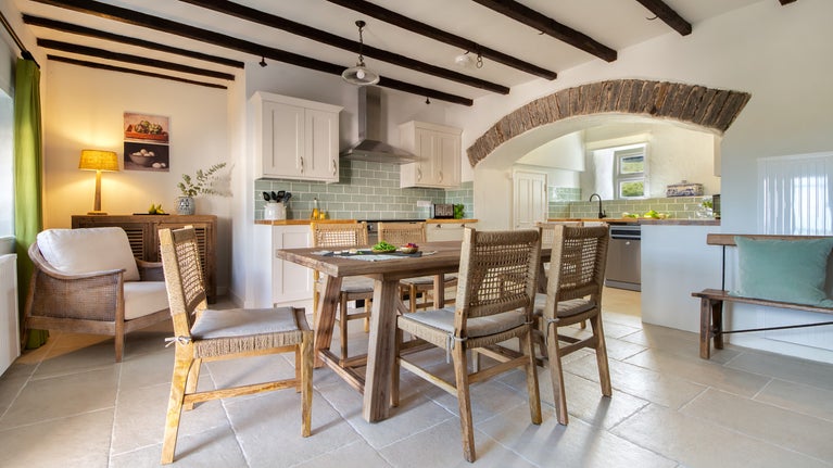 The kitchen with dining table for six and original beams and stone ceiling arch, at Newgale Wood Farm, Pembrokeshire